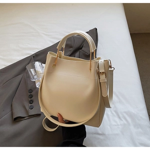 Detail of a creamy white bucket bag featuring a gold metal handle and a curved base