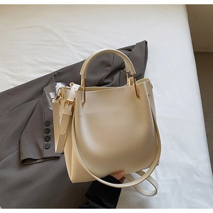 Close-up of cream bucket bag with metal handles and thin shoulder strap on grey blazer