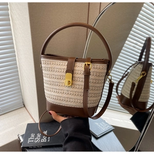 Detail of straw bucket bag with contrast leather trim and gold hardware in elegant setting