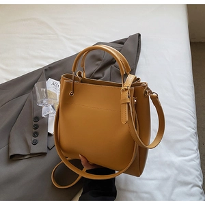Detailed view of ginger yellow leather bucket bag with top handle and metallic buckle