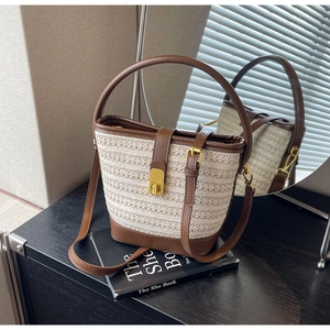 Detail of hand-woven straw bucket bag with brown leather trim and golden metal lock
