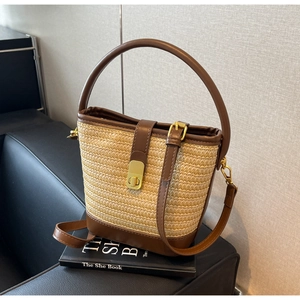 Detail of straw bucket bag featuring dark brown leather trim and vintage gold metal lock