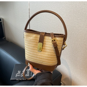 Detailed view of woven straw bucket bag with contrast brown leather trim and gold lock