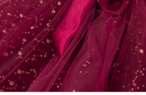 Dettaglio macro del tulle rosso vino con paillettes dorate e accenti di raso lucido