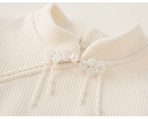 Details von Perlenknöpfen und Fransenquasten an einem cremefarbenen Strickkleid