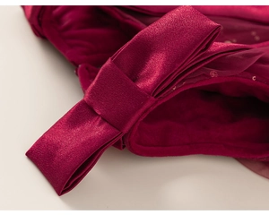 Dettaglio di un abito festivo in raso bordeaux con un elegante fiocco applicato