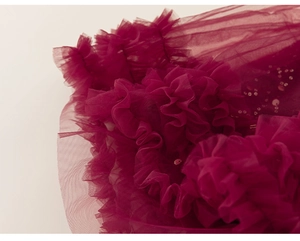 Dettaglio di balze in tulle bordeaux a strati con paillettes luccicanti sull'abito festivo