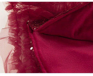 Dettaglio del tessuto in tulle bordeaux con fodera in pile e ricami di paillettes dorate