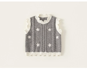 Close-up of cable knit girl's vest with white floral embroidery and scalloped trim