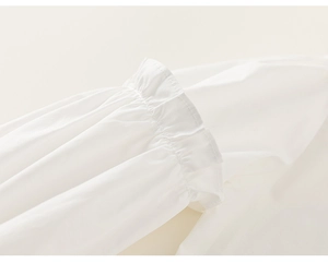 Détail des poignets à volants sur une blouse blanche à manches longues en tissu tissé