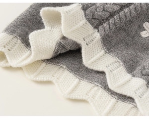 Close-up of grey cable knit fabric with white scalloped edge and floral embroidery