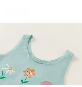 Détail du gilet en tricot vert menthe avec broderie de marguerites et de lys orange