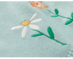 Détail de broderie florale avec marguerites blanches sur un gilet en maille enfant