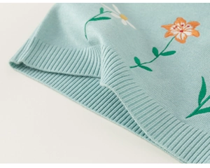 Vue détaillée du gilet en tricot bleu clair avec motifs de marguerites et bords côtelés