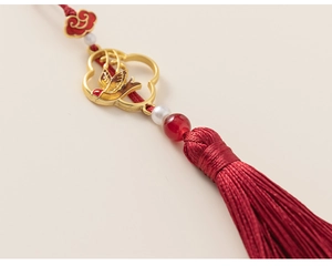 Détail macro d'un gland en soie rouge traditionnel avec une hirondelle dorée et perle