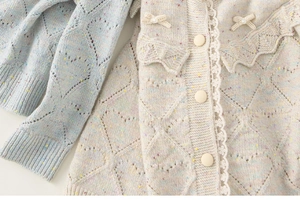 Detail van gebreid vest met kanten rand, parelknopen en een handgemaakte gebreide strik