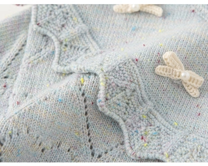 Detail van lichtblauw gebreid vest met schulpranden en parelmoer strikdecoratie
