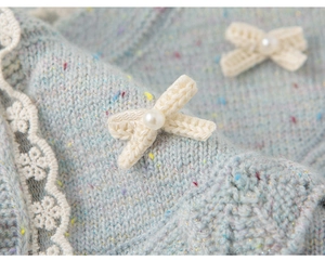 Detail van lichtblauw gebreid vest met kanten rand en strikjes met parelmoeren details