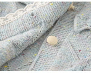 Detail van lichtblauw gebreid vest met kleurrijke spikkels en kantrandje