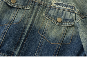 Detail of vintage denim jacket showing metal button and distressed alphabet patch embroidery