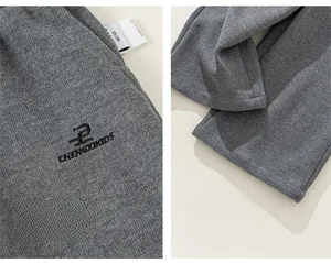 Detail view of grey knitted cotton trousers showing high-quality embroidery and cuff tailoring