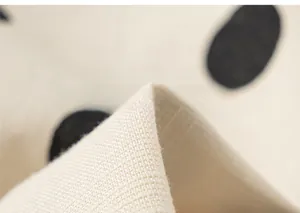 Detailed close-up of soft cotton-linen fabric with black polka dots on cream background