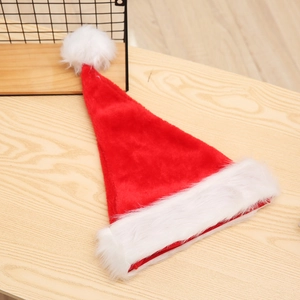 Detail of red plush Christmas hat with white faux fur trim on a wooden background