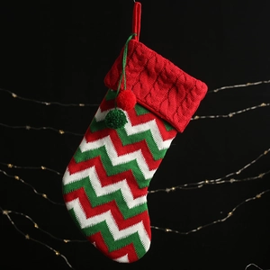 Knitted Christmas stocking with red, white and green wave patterns and plush pom-pom charms
