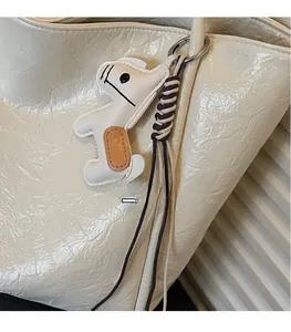 Detail of a white leather horse bag charm with woven strap on a textured tote bag