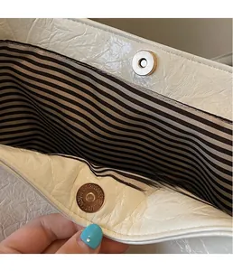 Detail of magnetic gold clasp and striped lining on an off-white wax leather tote bag