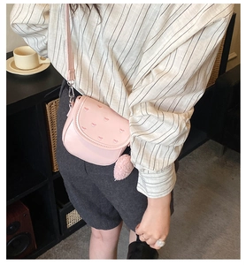 Detalle del bolso bandolera rosa con forma de corazón, bordado y un pompón suave
