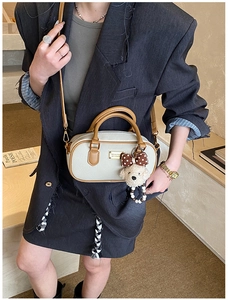 Detail of a mini Boston crossbody bag in cream and brown with a cute plush puppy charm