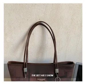 Close-up of brown bucket bag handle with leather logo tag and fine textured finish