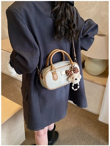 Detail of cream leather cylinder bag with brown trim and plush puppy charm on a model