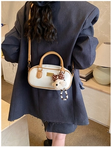 Detail of white lychee leather handbag with a plush teddy bear charm and gold emblem