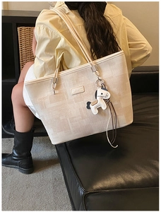 Detail of minimalist beige bucket tote bag featuring a leather patch and horse pendant charm