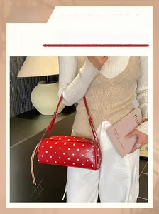 Close-up of red polka dot cylinder shoulder bag with leather tassel detail on model