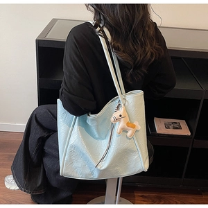 Detail view of light blue wrinkled tote bag with cute horse charm on shoulder of a model