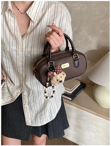 Detail of dark brown leather handbag with golden logo and cute bear doll charm accessory