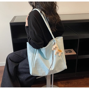 Light blue faux leather tote bag detail with a beige horse charm shown on shoulder