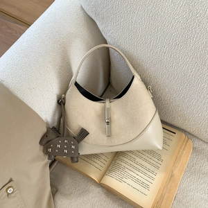 Detail of beige crescent hobo bag with silver buckle and pony charm on textured sofa