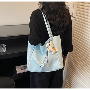 Detail of light blue faux leather tote bag with decorative horse charm and tassel fringe