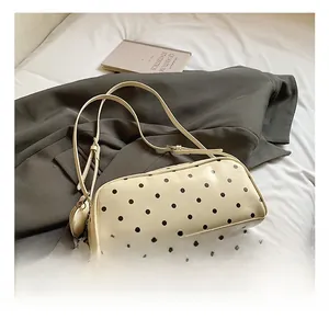 Detailed view of polka dot cylindrical shoulder bag on a minimalist white bedding setup