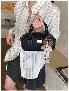 Close-up of black matte lychee texture handbag with golden plate and plush bear charm