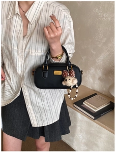 Detail of black cylindrical bowling bag with a cute teddy bear charm and gold logo plate