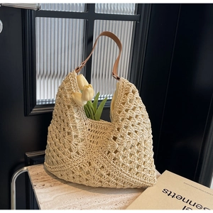 Close-up of hollow woven hollow design on beige straw tote bag with brown leather strap