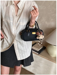 Detail of black faux leather handbag featuring gold logo plate and cute teddy bear charm
