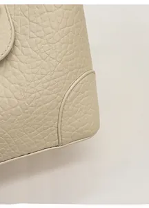 Macro detail of creamy beige bucket bag showing rich lychee grain leather and fine stitching