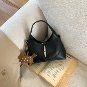 Close-up of black leather pleated bag with silver lock and horse charm on a white sofa
