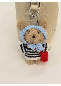 Detail of cute brown plush bear charm with blue knit sweater on light beige bucket bag